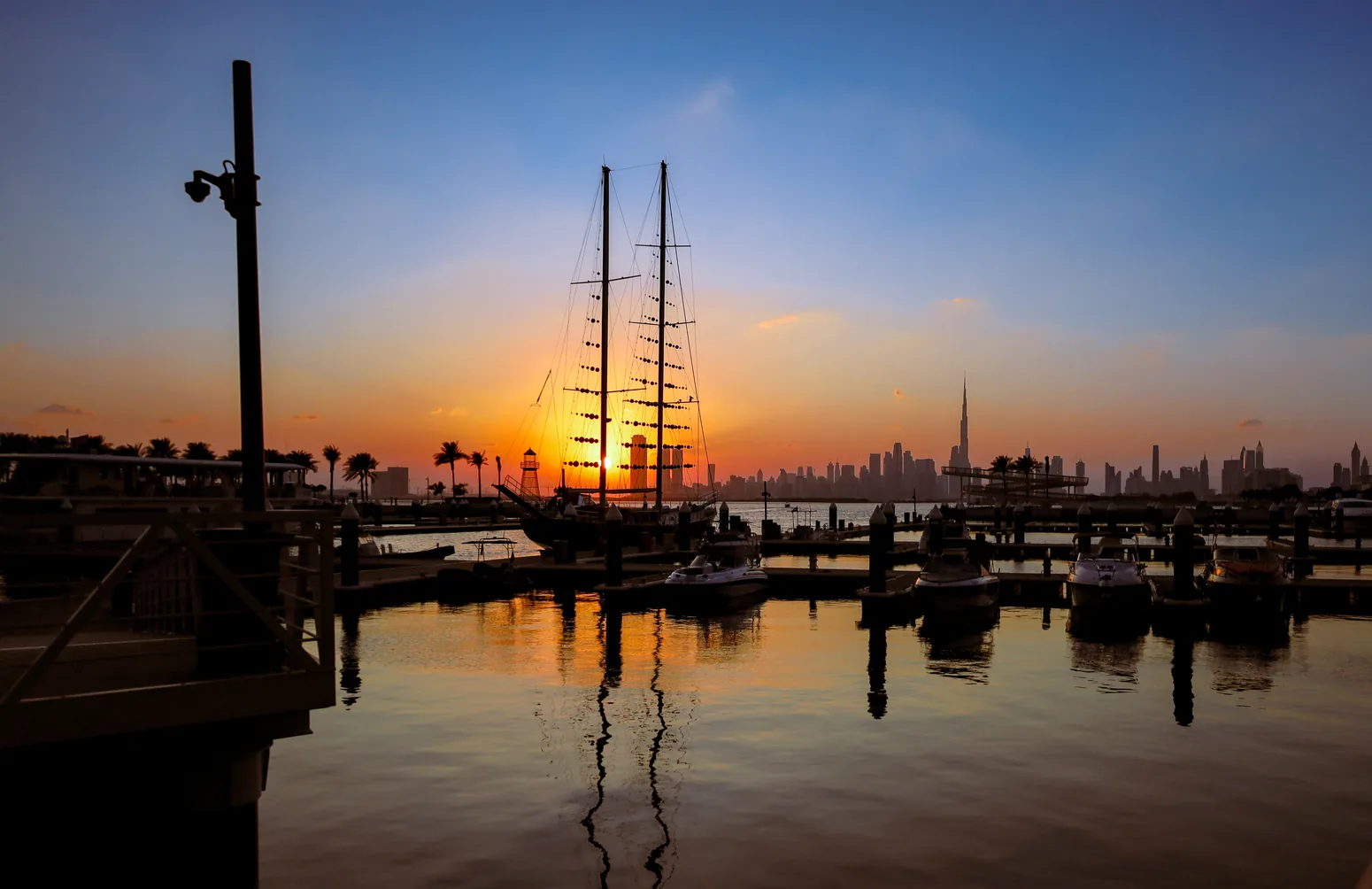 Coucher de soleil sur Dubai Creek Harbour : bateaux sur le Creek et skyline de Dubaï à l'arrière-plan.